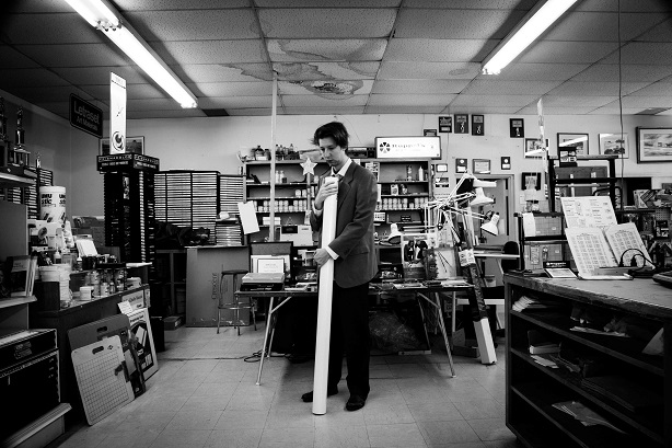 Emmanuel Schwartz tenant un rouleau de papier dont se servait Alfred McMoore pour faire ses tableaux, dans le magasin même où il s’approvisionnait. Ces grands rouleaux de papier font 42 pouces (107 centimètres) de hauteur.