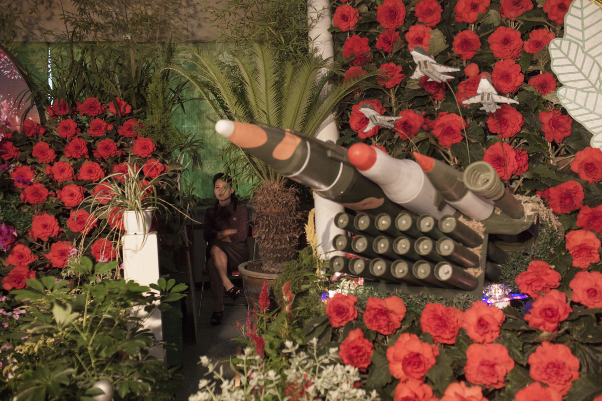 A North Korean woman sits next to models of military weapons at a festival for the "Kimilsungia" and "Kimjongilia" flowers, named after the country's late leaders, in Pyongyang, North Korea, Wednesday, July 24, 2013. The exhibition was held to mark the 60th anniversary of the end of the Korean War on July 27.